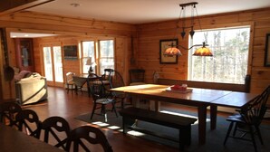 Interior de una cabaña de madera con comedor, paredes de madera y ventanas amplias.