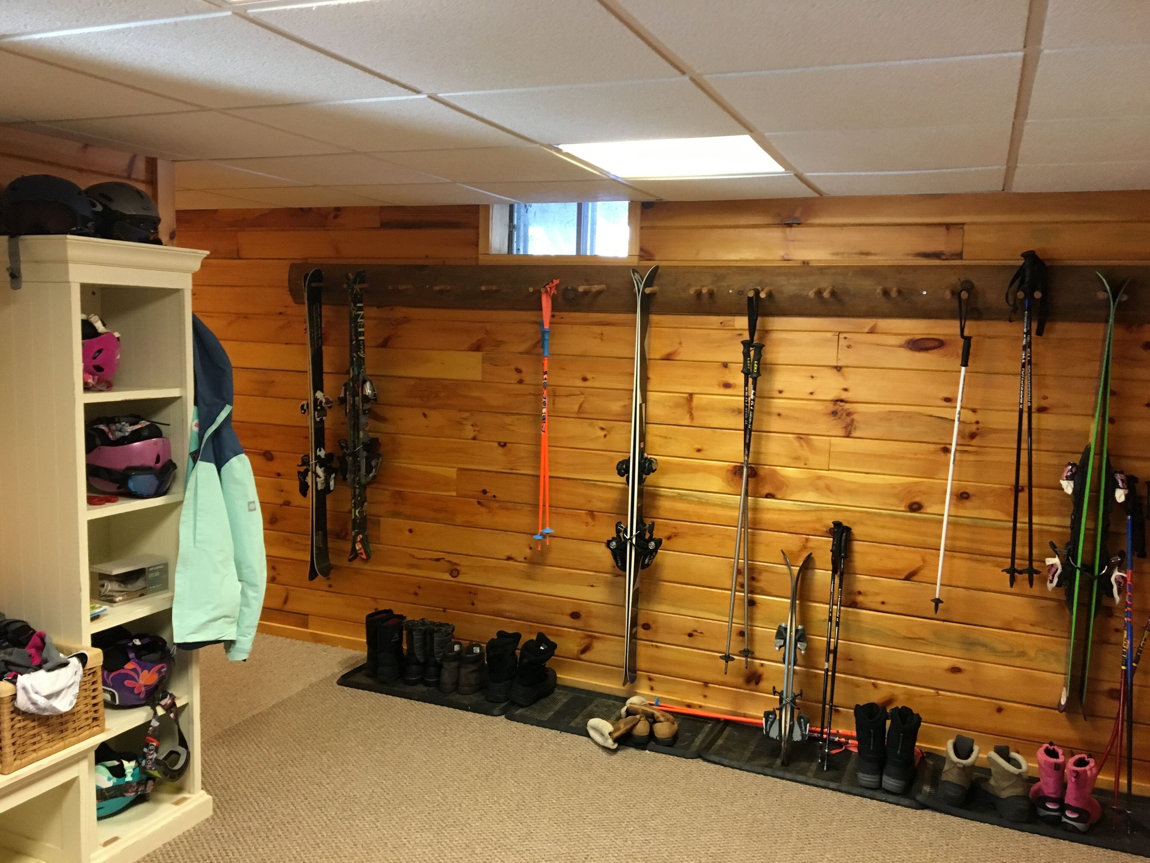 A ski storage room with skis and ski poles on racks, a shoe rack with boots, and a wooden wall.