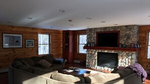 Una sala de estar acogedora con chimenea de piedra, paredes de madera y un amplio sofá modular.