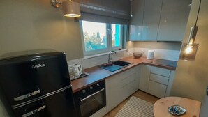 A compact kitchen with a black Amica refrigerator, a sink, and a small dining area with a round table. - Apartament plaża 41 bros (Gdansk)