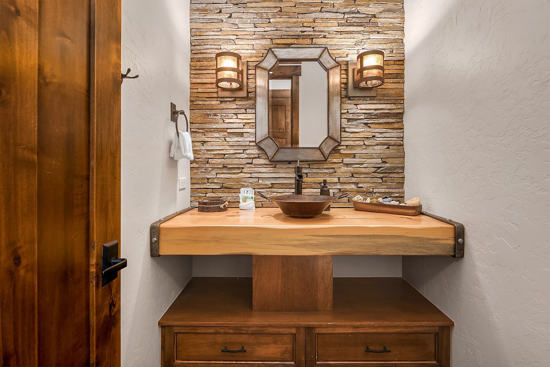 A bathroom with a stone wall, a wooden vanity, a mirror, and two wall-mounted lights.