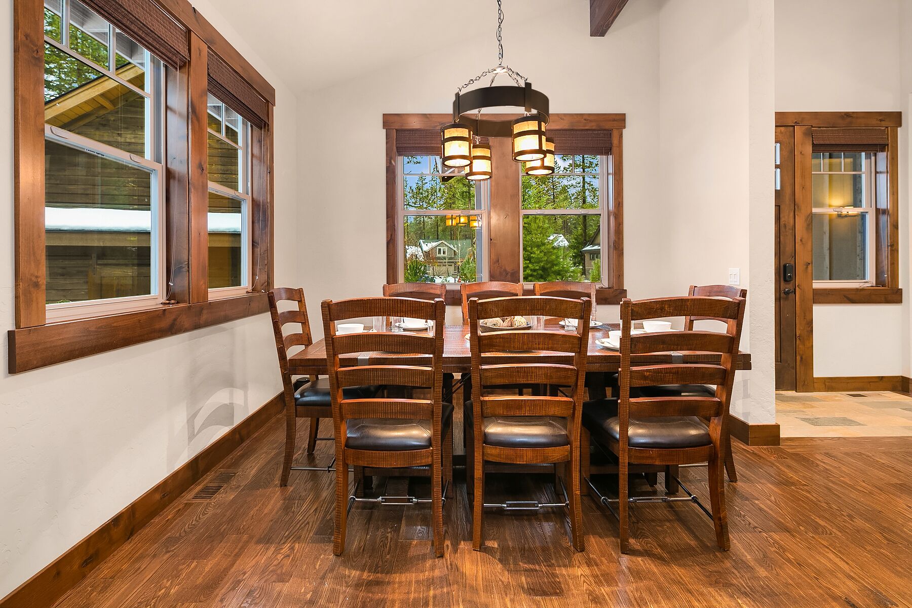 Un comedor con mesa y sillas de madera, ventanas amplias y una lámpara colgante.