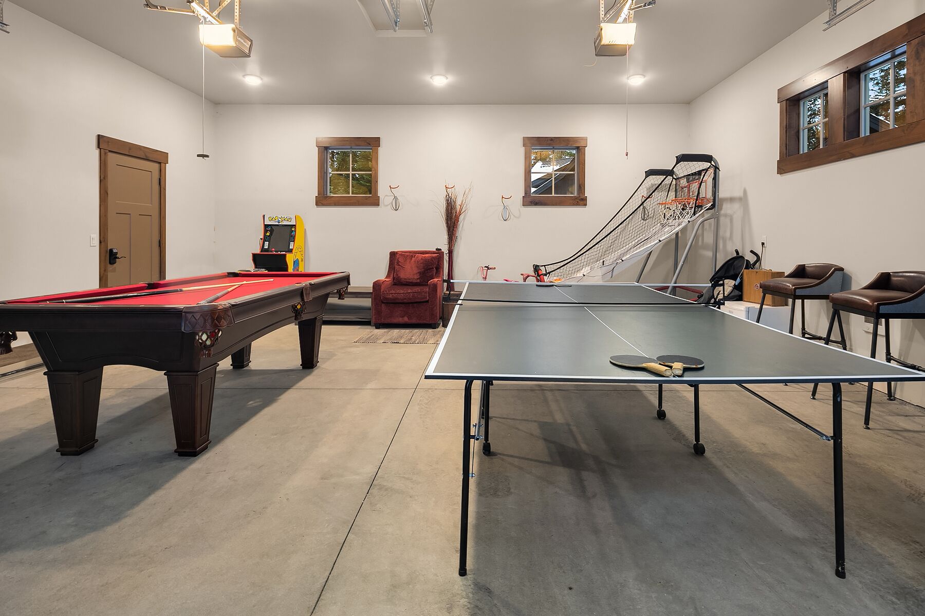 Una sala de billar con mesa de pool, mesa de snooker y mesa de ping pong. Hay dos ventanas con marcos de madera y una puerta.