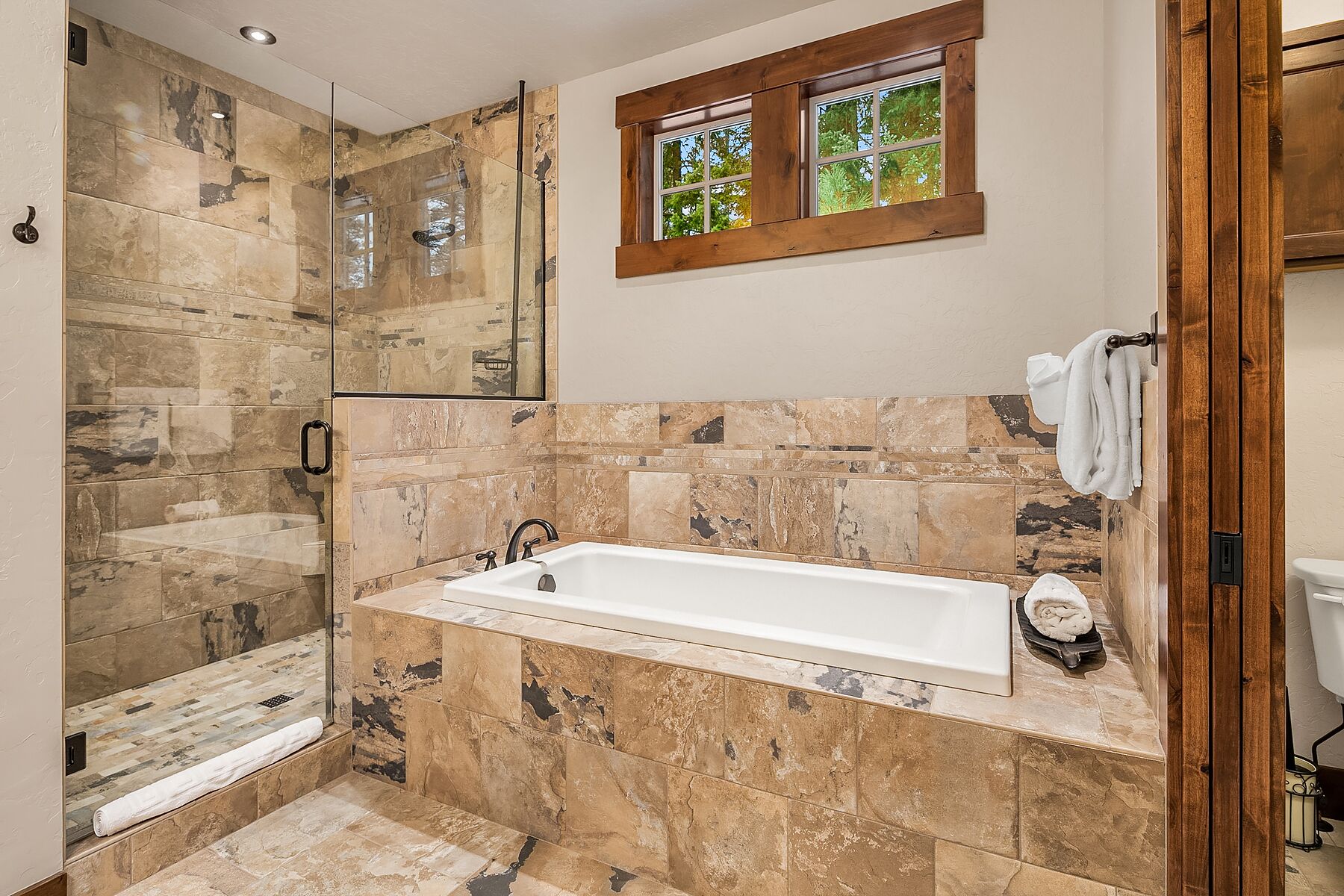 Un baño con ducha de piedra, bañera y ventana con vistas a árboles.