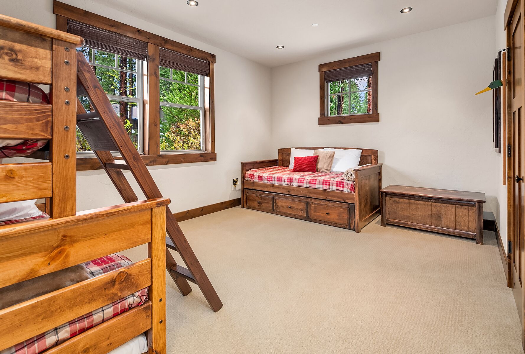 A bedroom with a loft bed, a wooden bench, and a small table. There are two windows providing natural light.