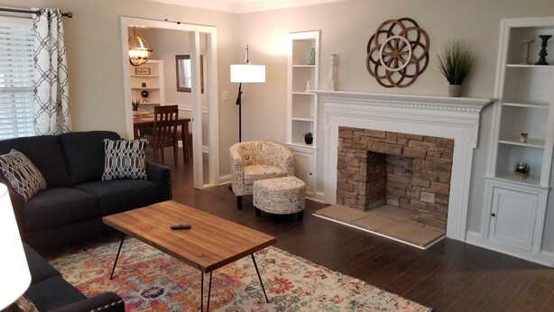 A living room with a black sofa, patterned ottoman, wooden coffee table, and a fireplace. - Clean & Safe in Downtown Morristown (Morristown)