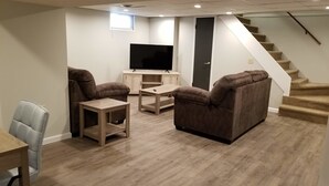 A modern living room with a flat-screen TV, two brown sofas, a small wooden coffee table, and a staircase leading to an upper level. - Clean & Safe in Downtown Morristown (Morristown)