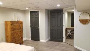 A bedroom with a wooden dresser, two dark doors, a round mirror, and a bed. - Clean & Safe in Downtown Morristown (Morristown)