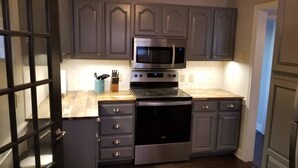 A kitchen with grey cabinets, a stainless steel microwave, an oven, and a countertop with a knife block. - Clean & Safe in Downtown Morristown (Morristown)