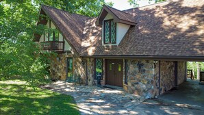 A two-story stone house with a stone porch and a wooden deck. - Lake Reunion location, private dock/slip/lily pad. 3 acres, hiking, fire pit, walk to Bagnell Dam (Lake Ozark)