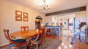 A dining area with a wooden table and chairs, a chandelier, and a kitchen in the background. - Lake Reunion location, private dock/slip/lily pad. 3 acres, hiking, fire pit, walk to Bagnell Dam (Lake Ozark)