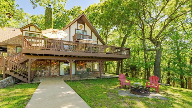 A two-story cabin with a balcony, stone foundation, and a fire pit area. - Lake Reunion location, private dock/slip/lily pad. 3 acres, hiking, fire pit, walk to Bagnell Dam (Lake Ozark)