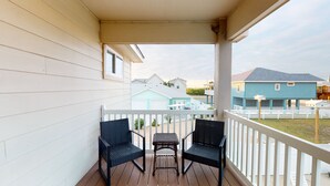 Une véranda avec deux fauteuils en osier et une petite table, donnant sur un quartier résidentiel avec des maisons.