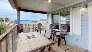 Un espace extérieur abrité, doté d’une terrasse en bois, d’une table avec des chaises et offrant une vue sur l’océan.