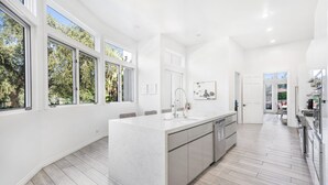 A modern kitchen with a large island, white cabinetry, and a view of the outdoors.
