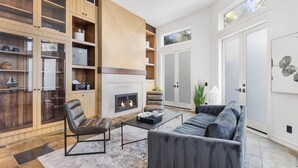 A modern living room with a fireplace, leather chairs, a sofa, and built-in wooden shelving.