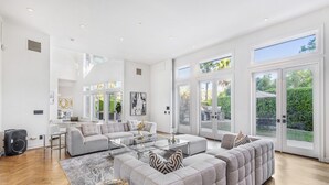 A spacious living room with a large sectional sofa, a glass coffee table, and a view of the outdoors through large sliding glass doors.