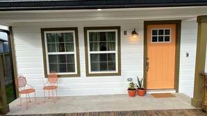 Ein Haus mit Veranda, zwei Fenstern, einer Tür und zwei Blumentöpfen.