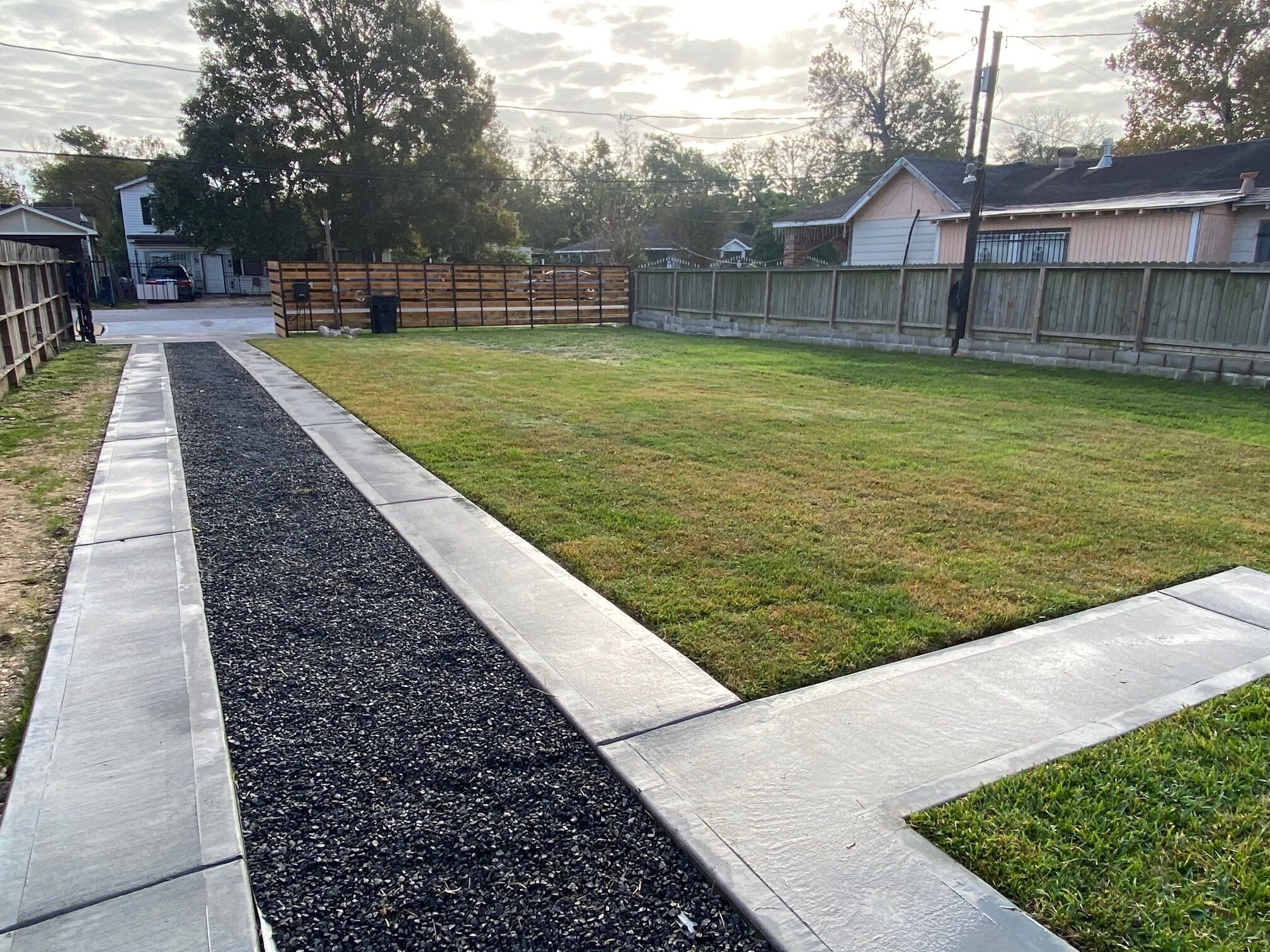 A backyard with a concrete pathway, a grassy area, and a wooden fence.