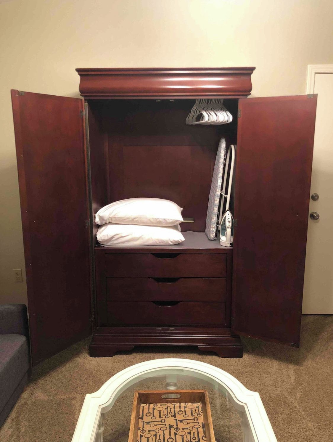 Um guarda-roupa de madeira com espelho, cabideiro e uma cama com almofadas.