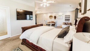 A bedroom with a wooden bed, a TV mounted on the wall, a ceiling fan, and a small table with chairs.