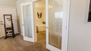 A room with a door leading to a bathroom, a mirror, and a wall-mounted decoration.