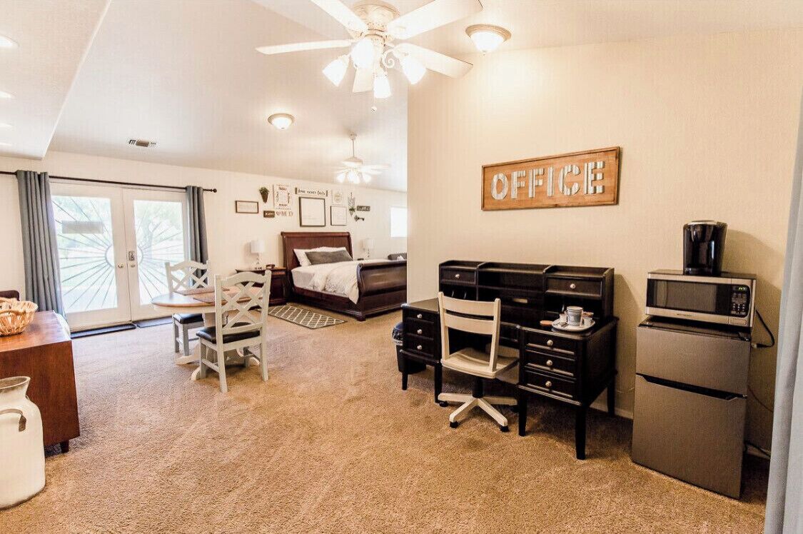 A compact, well-lit room with a ceiling fan, a bed, a desk with a chair, a refrigerator, and a microwave.