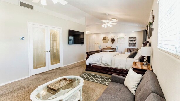 A bedroom with a bed, a TV, a ceiling fan, and a window.