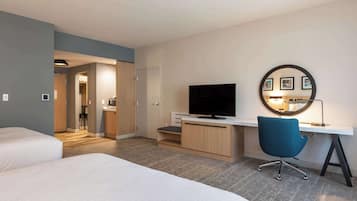 A hotel room with a bed, a desk with a chair, a television, and a mirror with pictures.