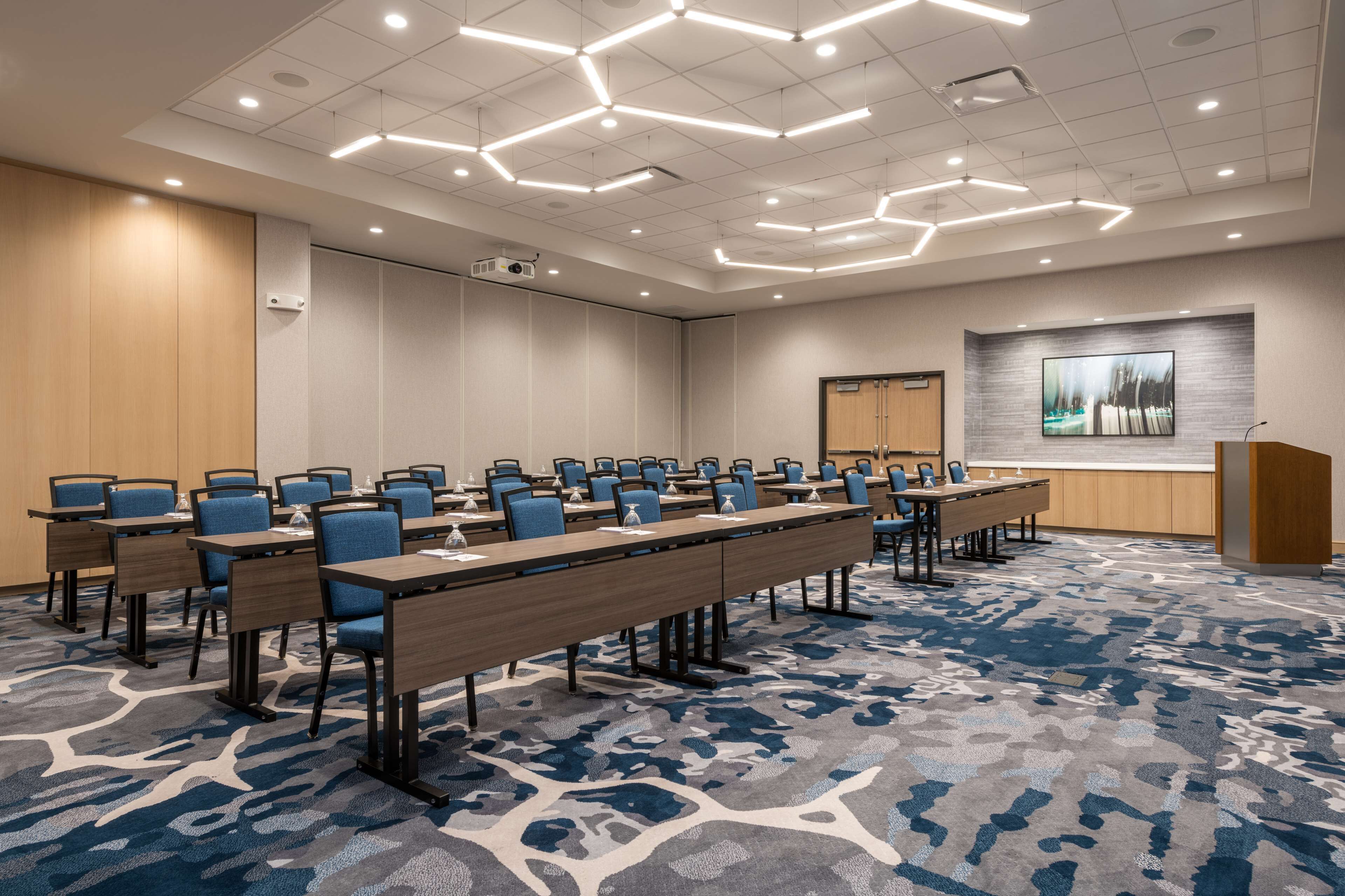 A conference room with a long table, multiple chairs, a podium, and a projector screen.