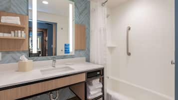 Une salle de bain moderne avec un grand miroir, un lavabo, une douche équipée d’une barre d’appui et des serviettes soigneusement pliées.