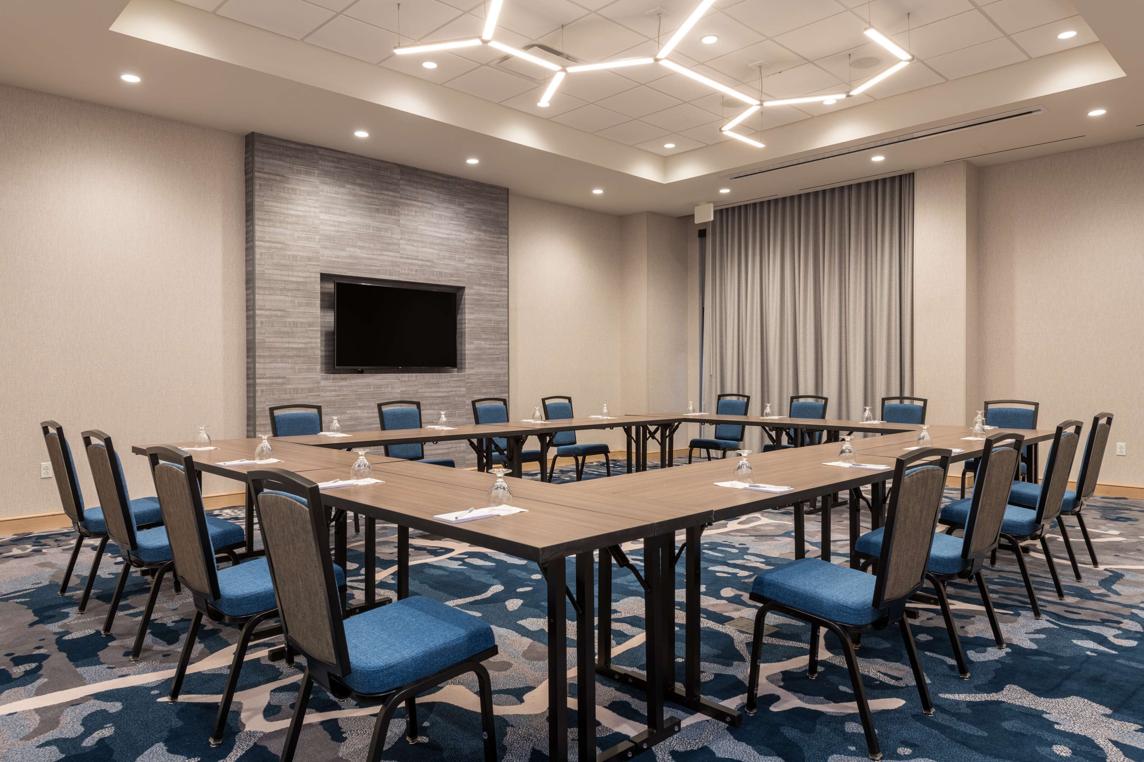 A conference room with a long table, blue chairs, a flat-screen TV, and a patterned carpet.