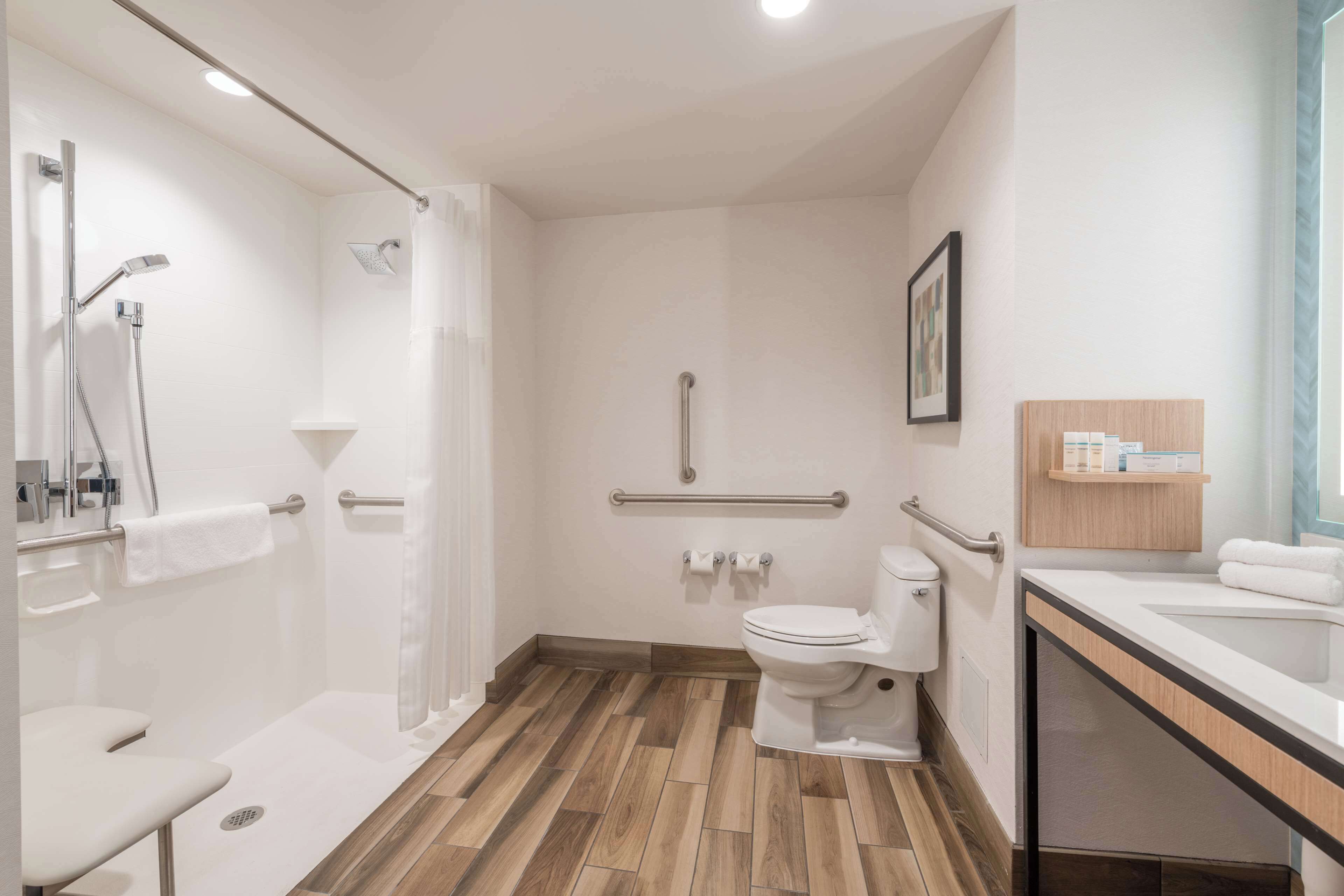 Une salle de bain moderne équipée d’une douche, de toilettes et d’un lavabo, avec un sol en bois et des murs blancs.