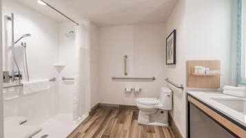 Une salle de bain moderne équipée d’une douche, de toilettes et d’un lavabo, avec un sol en bois et des murs blancs.