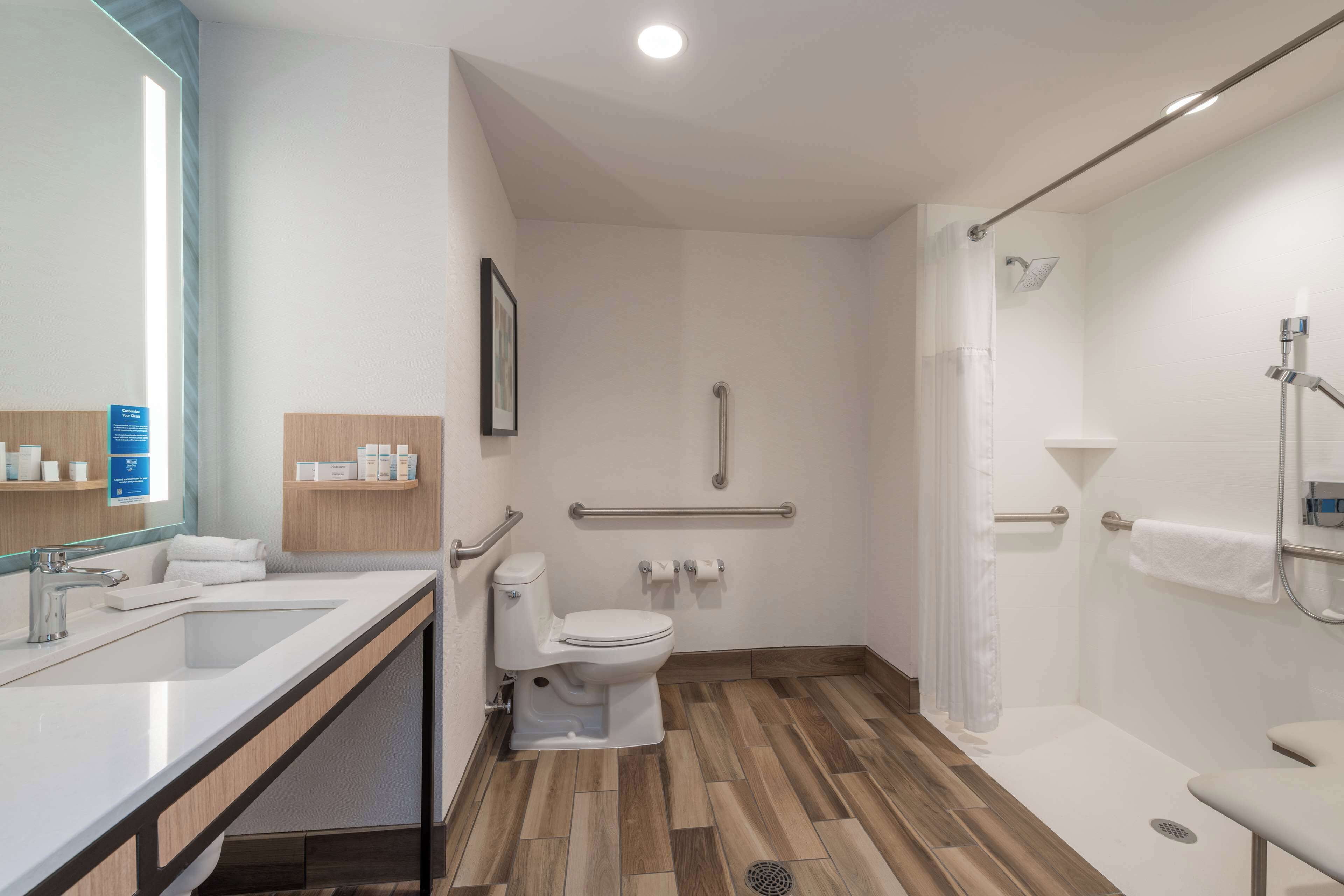 Ein modernes Badezimmer mit Waschbecken, Toilette, Dusche und Haltegriffen.