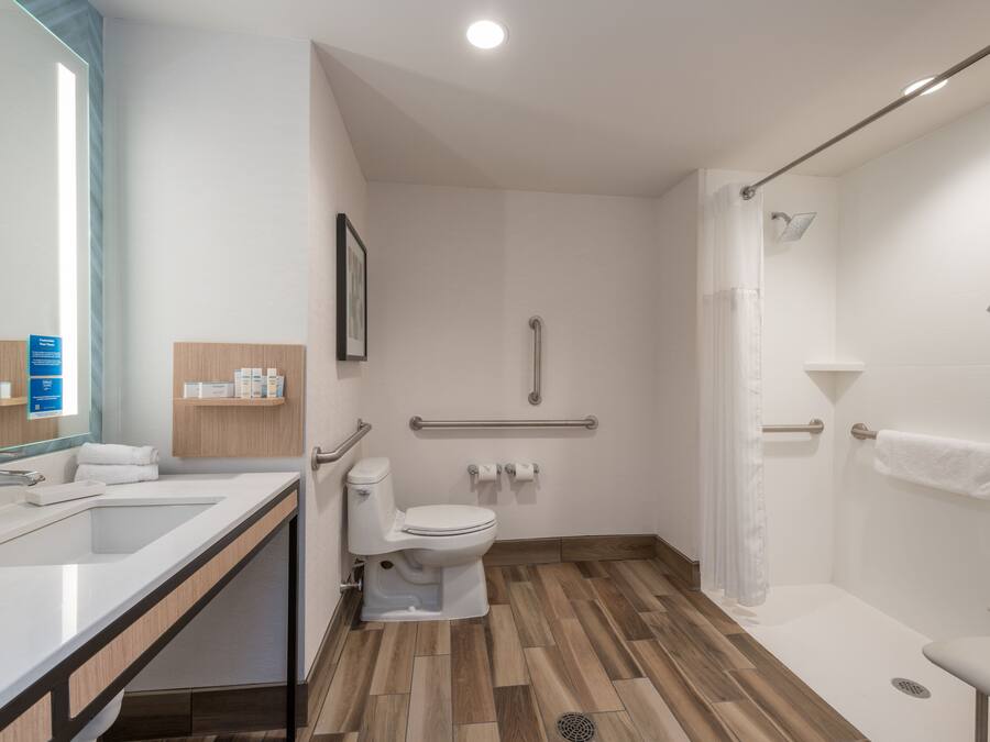 A modern bathroom with a sink, toilet, shower, and grab bars.
