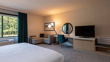 Habitación de hotel con una cama grande, un escritorio con computadora, un televisor y una ventana con cortinas.