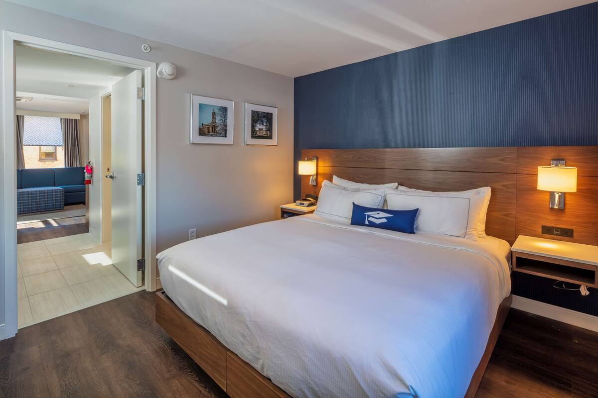 A hotel room with a large bed, two bedside lamps, a wooden headboard, and a door leading to a balcony.
