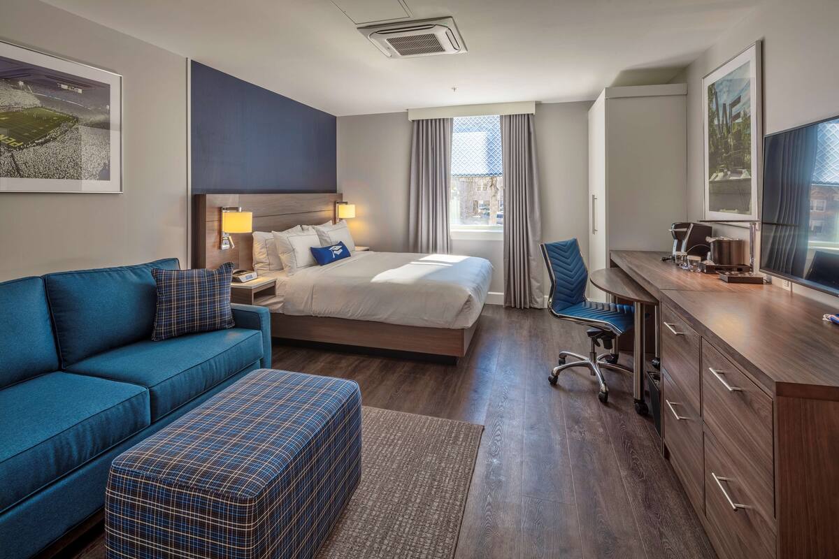 A modern hotel room with a bed, a sofa, a desk, and a television.