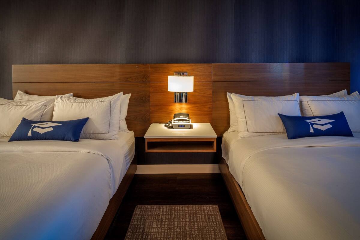 A hotel room with two beds, a nightstand with a lamp, and a wooden headboard.