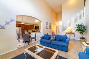 A living room with a blue sofa, a coffee table, and a dining area with chairs and a table.