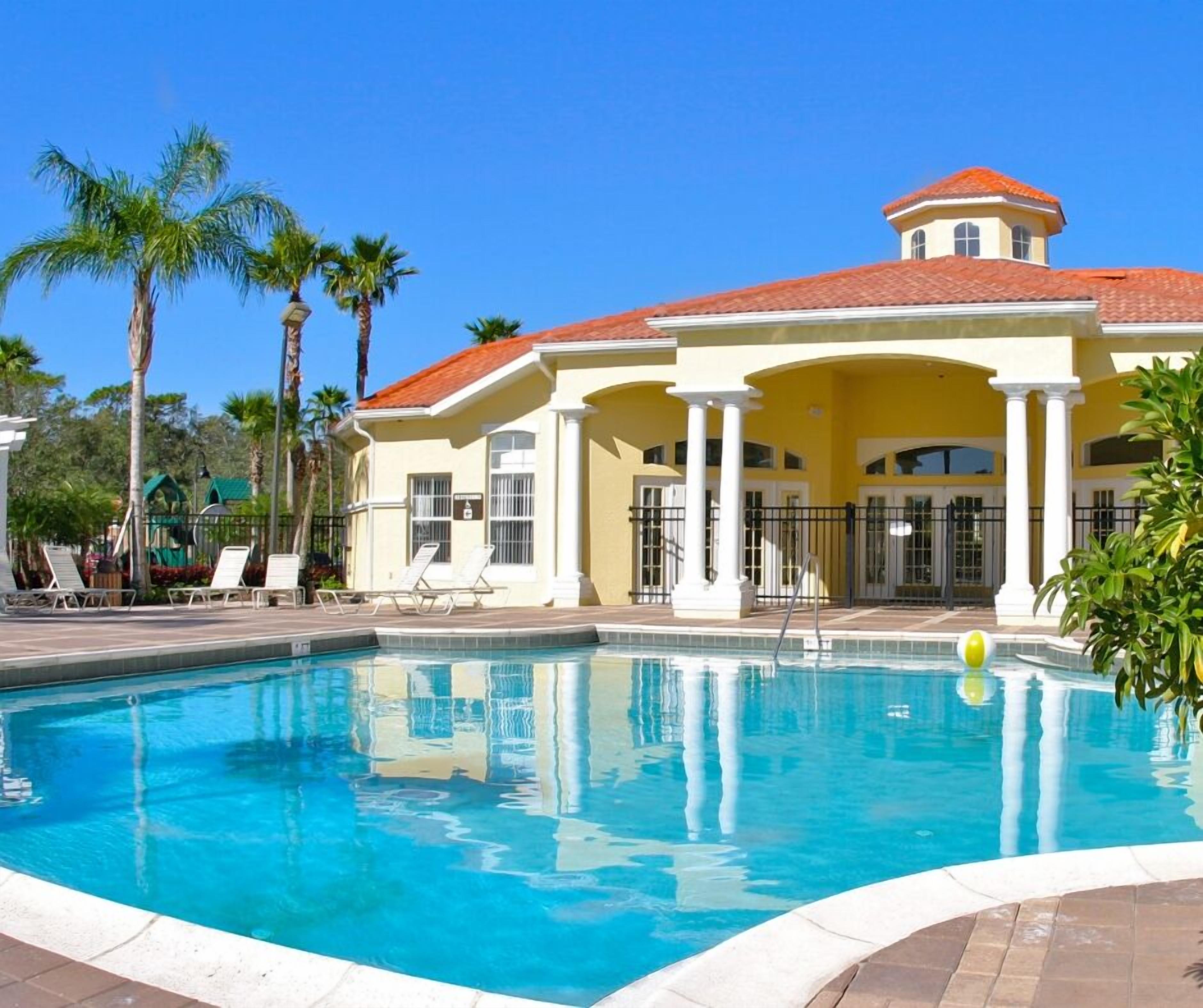 A pool area with a clear blue pool, white lounge chairs, and palm trees.