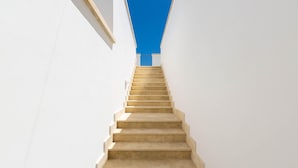 Un escalier droit aux marches de couleur beige, montant vers le haut entre deux murs blancs.