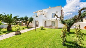 Une villa blanche dotée d’une grande pelouse, d’un espace salon extérieur et d’une pergola.