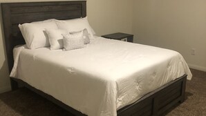 A bedroom with a dark wooden bed frame, white bedding, and a small bedside table. - Newly built property (Bakersfield)