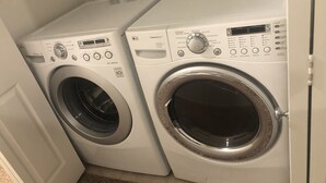 Two front-loading washing machines in a laundry room with a door on the left and a control panel on the right. - Newly built property (Bakersfield)