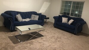 A living room with two blue sofas, a glass coffee table, and a window with blinds. - Newly built property (Bakersfield)