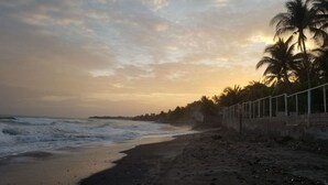 A beach with waves, palm trees, and a fence along the shore. - Stunning and enjoyable beach house! (la libertad)