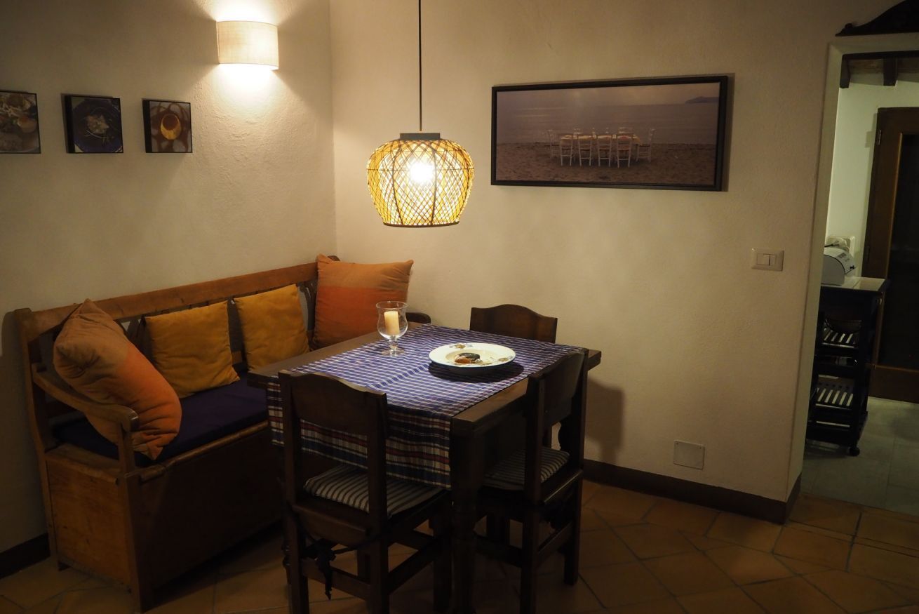 Ein gemütlicher Essbereich mit Holztisch, Stühlen und einer Bank. Über dem Tisch hängt eine Leuchte, und an der Wand hängt ein gerahmtes Bild.