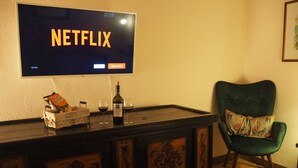 A room with a television displaying 'NETFLIX', a bar area with a bottle of wine, glasses, and snacks. - Only ten minutes walk to the golf course and still very quiet (Saturnia)